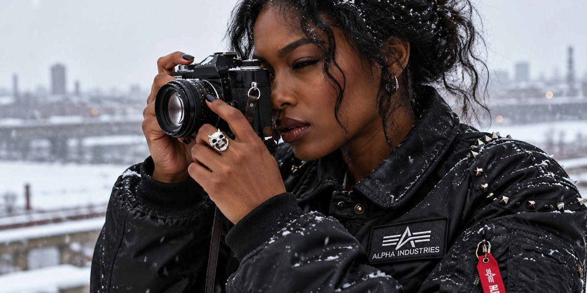 Woman in a studded black flight jacket and a skull ring taking a photo in the snow