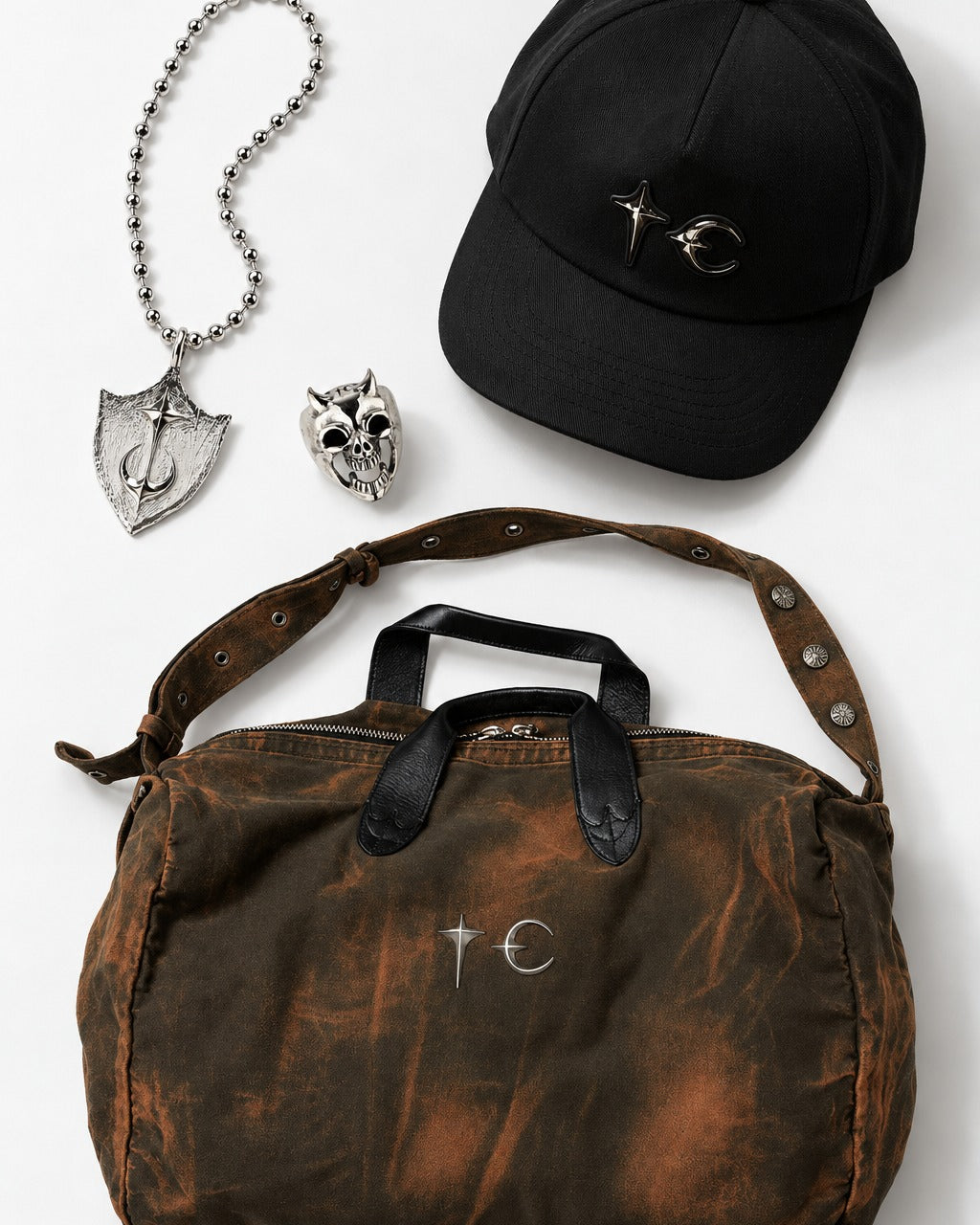 Shield necklace, skull ring, canvas bag and cap laid flat