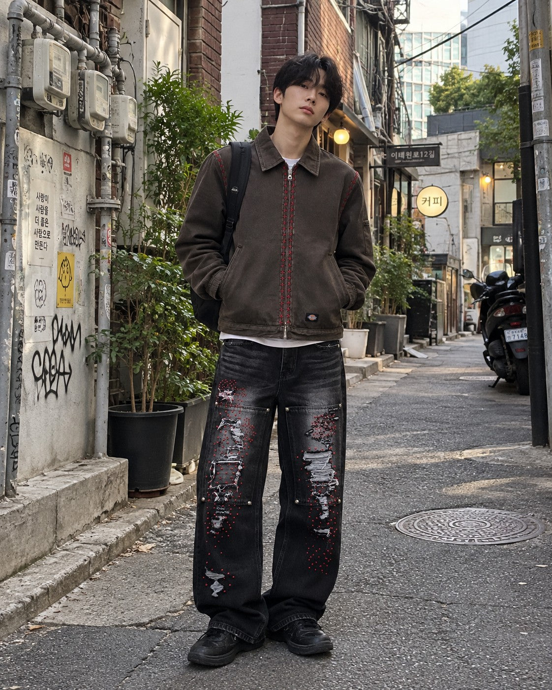 Man in a brown work jacket and black double-knee jeans standing in a Seoul alley